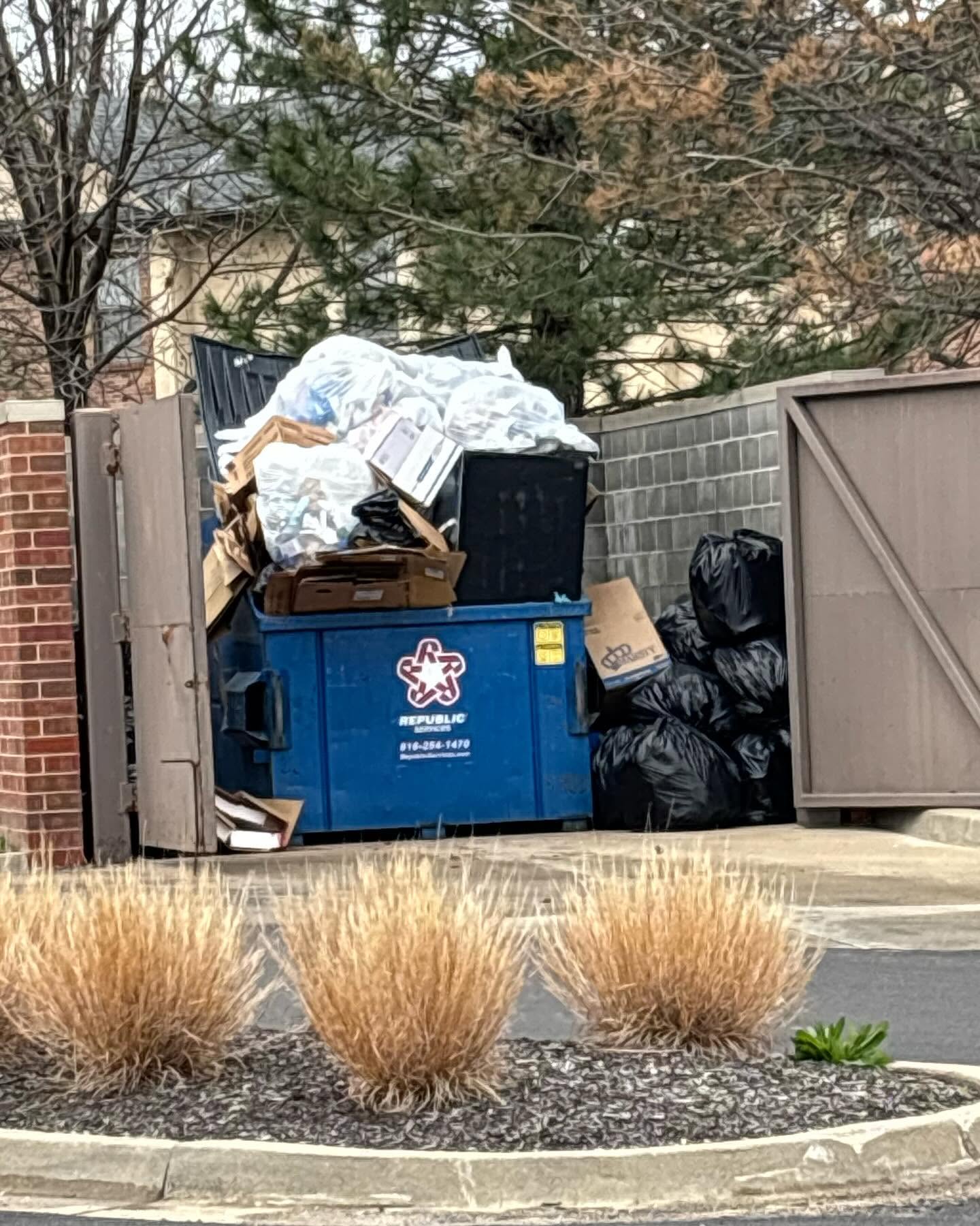 Overflowing apartment dumpster corral with bulk trash and bags